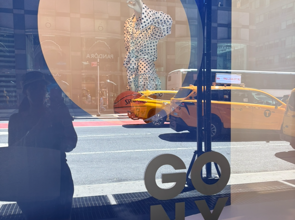 Bloomingdale’s NYC window display celebrating the New York Knicks championship with “GO NY GO” artwork, yellow taxis, and Manhattan street reflections.